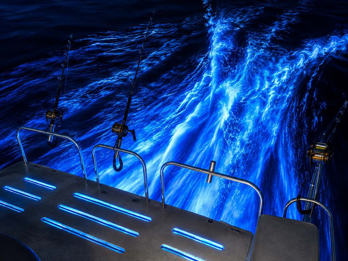 Underwater blue LED lighting illuminating wake and water behind offshore fishing boat at night